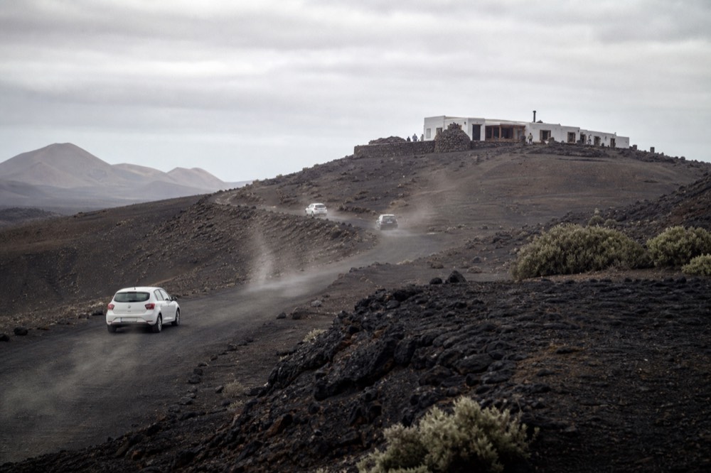 A volcanic landscape in Lanzarote with black ash fields and a low visitor building