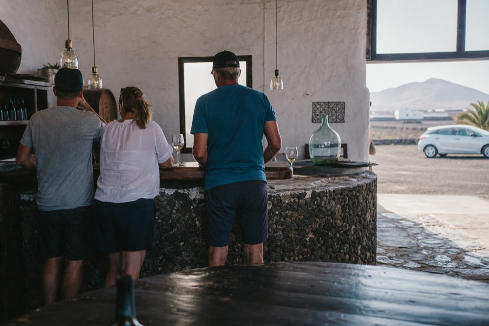 A small group tasting glasses of white wine at a wooden bar inside a Lanzarote winery