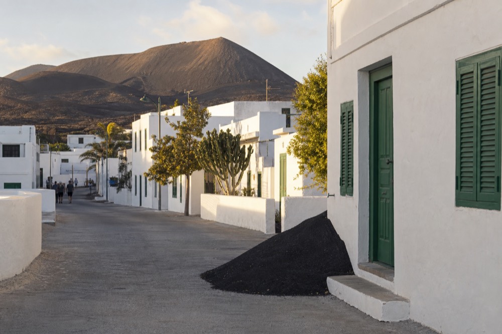 Whitewashed village street with green shutters and volcanic hills behind